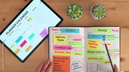 Businessman organizing work and home activities, writing appointments on a paper notebook and checking a digital tablet calendar, sitting at a wooden desk with plants
