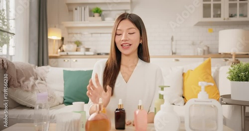 POV webcam view of Asian woman beauty influencer, content creator smiling while presenting skincare products to camera at home. vlog self care product review. Gen Z lifestyle social media trends.