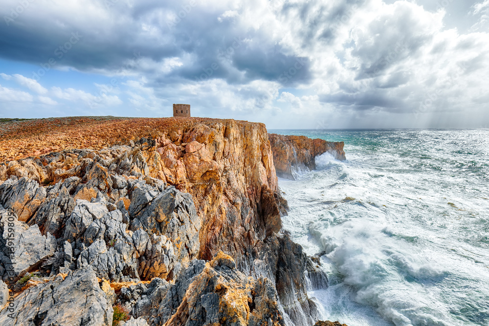 Attractive view of cliffs in valley Cala Domestica with old tower and storm on the sea