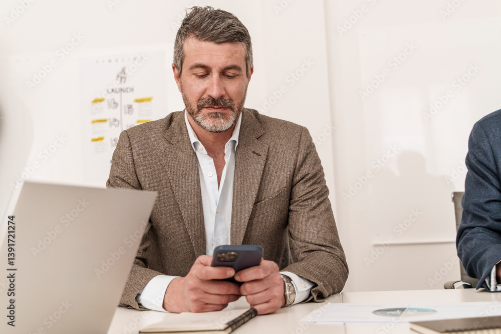 Fototapeta premium Senior businessman checking smartphone during office meeting