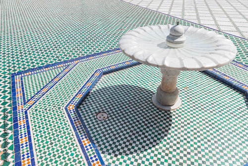 Obraz na płótnie White marble fountain is standing on a checkered mosaic floor with geometric patterns, showcasing traditional moroccan craftsmanship w salonie