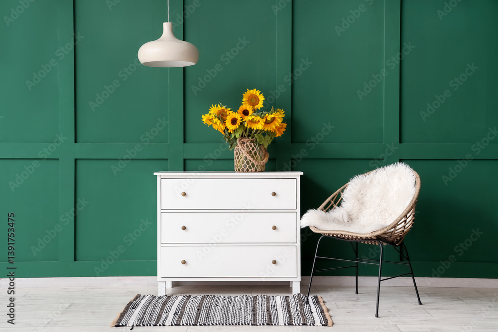 Vase with beautiful sunflowers on chest of drawers and cozy armchair near green wall