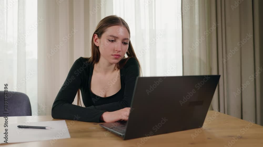 Young woman working at laptop at home, focused and concentrated at wooden table