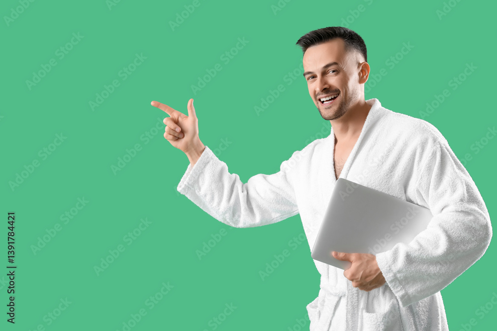 Happy young man in bathrobe with laptop pointing at something on green background Happy young man in bathrobe with laptop pointing at something on green background