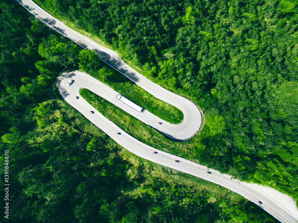 Aerial view of winding road in green forest with car, semi-trailer truck and motorcycles in Italy