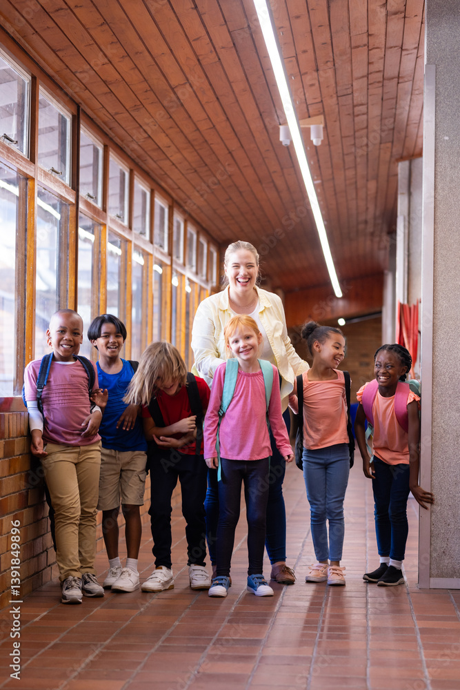 Female teacher with diverse group of school children standing in hallway, smiling together