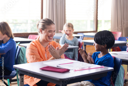 Obraz na płótnie Female teacher and boy clapping hands together in school classroom, smiling and engaged w salonie