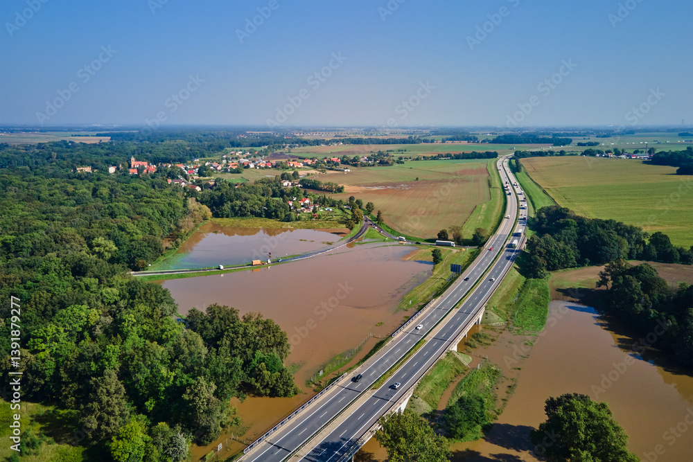 Aerial view of flooded fields and submerged rural road near busy highway. Concept of climate impact, transportation disruption and natural disaster