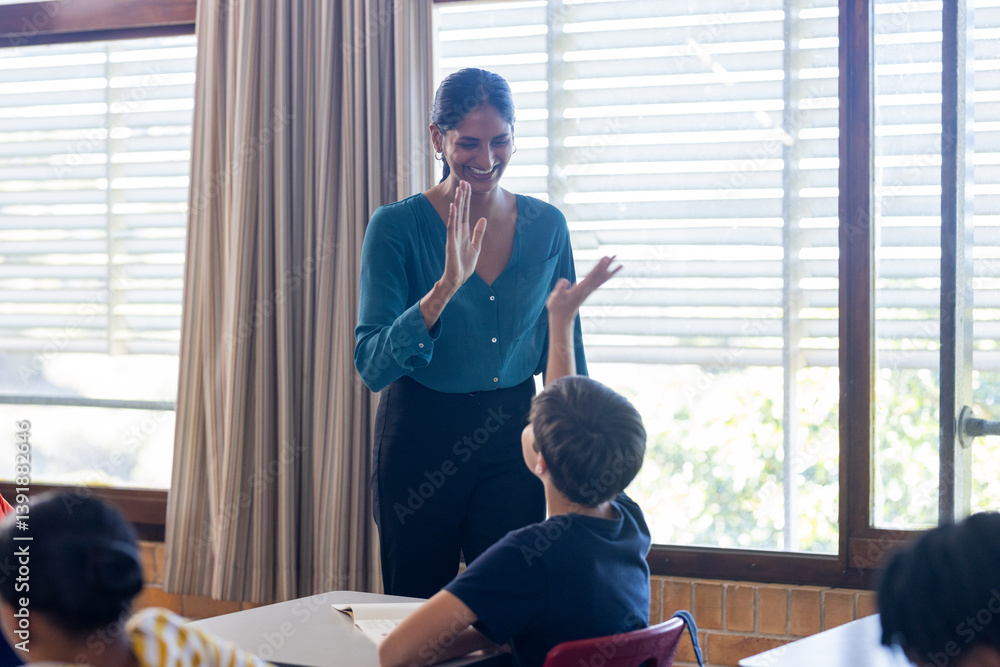 In school, Indian female teacher giving high-five to student in classroom, smiling and interacting