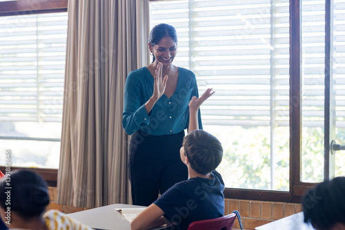 In school, Indian female teacher giving high-five to student in classroom, smiling and interacting