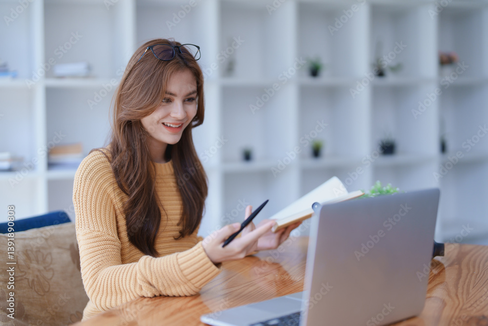 Smiling young woman engaged in a joyful online e-learning video call, gestu while holding a book with headphones on a wooden table nearby Smiling young woman engaged in a joyful online e-learning video call, gestu while holding a book with headphones on a wooden table nearby