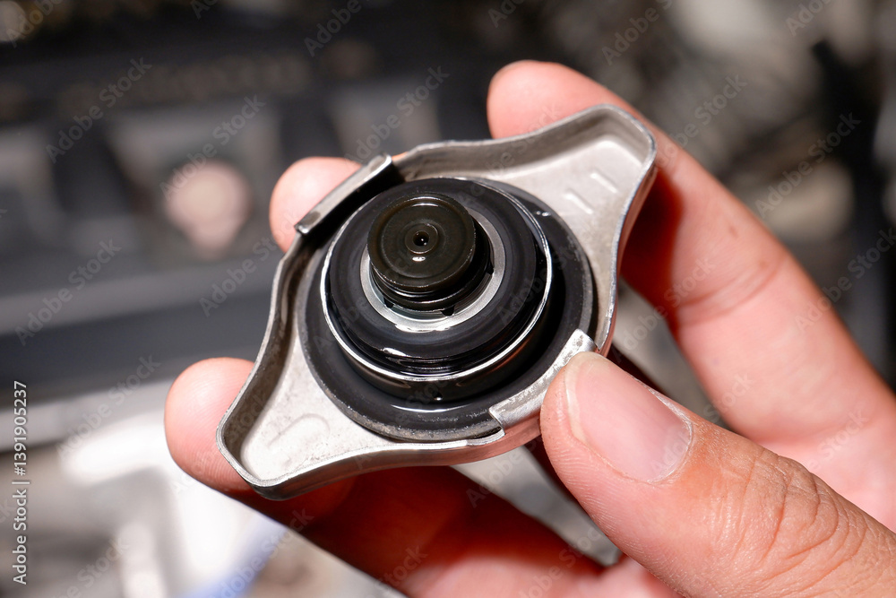 Car radiator cap, A hand holds a silver car radiator cap. Automotive maintenance and cooling system part.