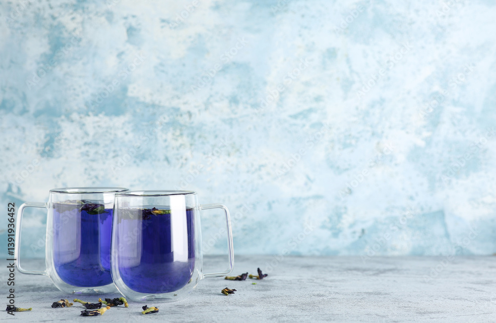 Cups of butterfly pea flower tea on blue grunge background with space for text