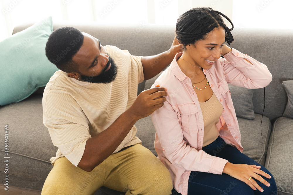 Happy couple sitting on sofa, man helping woman with necklace, smiling, at home Happy couple sitting on sofa, man helping woman with necklace, smiling, at home