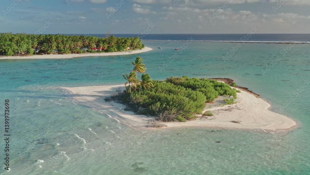 Vivid turquoise coral reef waters surround small, uninhabited island with palm trees, sand shore beach and gentle waves. Serene tropical paradise. Exotic travel getaway background. Aerial static shot