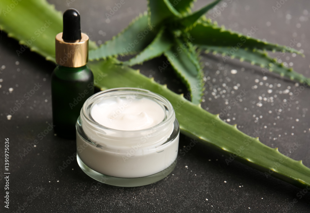 Bottle of cosmetic oil and jar of cream with aloe vera leaves on black background, closeup