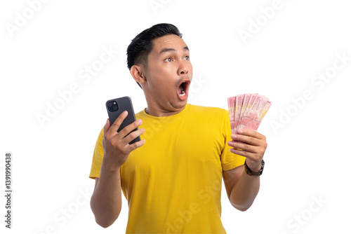 Excited handsome Asian man holding money and mobile phone, looking at copy space with shocked expression isolated on transparent background photo