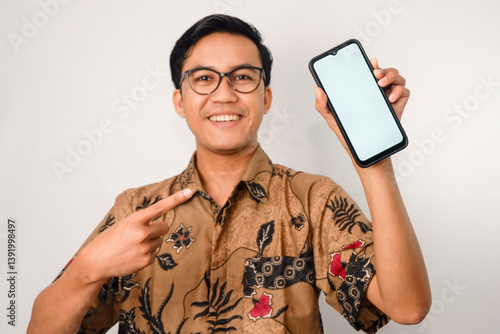 pria asia dengan wajah tersenyum memakai baju batik dan kacamata, dan tangan menunjuk ke smartphone
