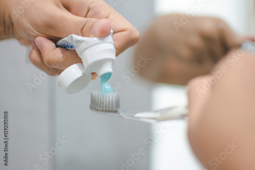 Hand Squeezing Toothpaste Onto Toothbrush in Bathroom Setting