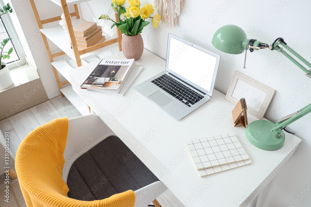 Blank laptop and vase with spring flowers on desk in light office