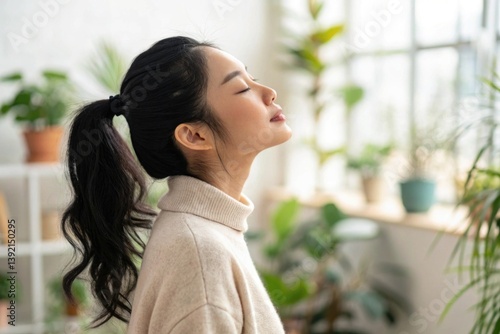 Obraz na płótnie Young woman relaxing at home with closed eyes, enjoying fresh air and positive energy in a bright, plant-filled indoor environment w salonie
