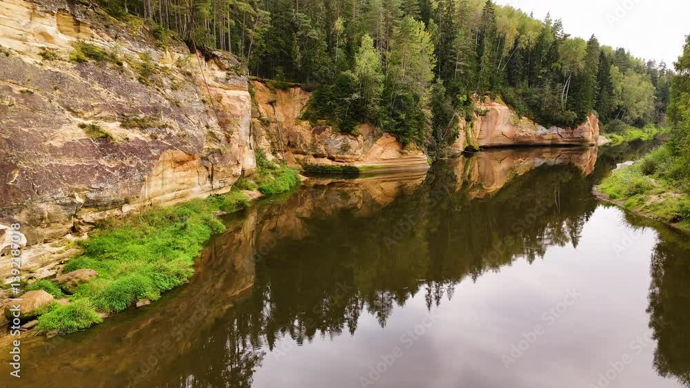 Sandstone cliffs in Gauja National Park reflected in the calm Gauja River in Latvia. Sandstone cliffs in Gauja National Park reflected in the calm Gauja River in Latvia.