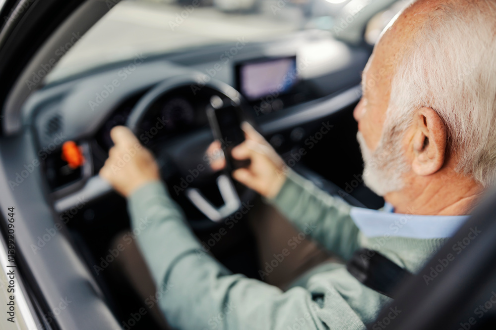Rear view of an old man driving a car and using cellphone in traffic. Rear view of an old man driving a car and using cellphone in traffic.