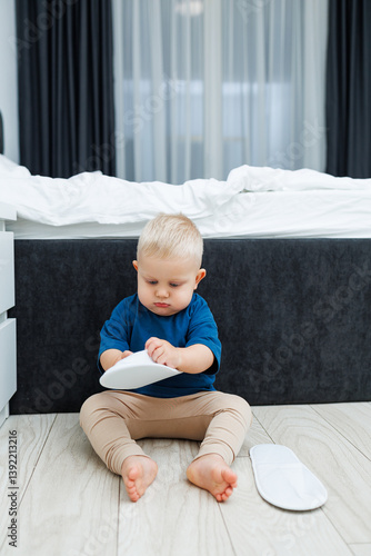 Obraz na płótnie Cute blond toddler boy in blue t-shirt running in spacious hotel room. Toddler boy in comfortable hotel room resting after travel. Child at home sitting on floor w salonie