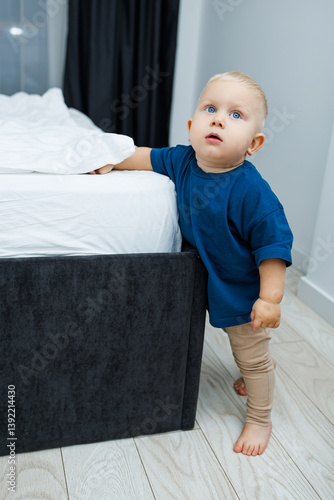 Obraz na płótnie Cute blond toddler boy in blue t-shirt running in spacious hotel room. Toddler boy in comfortable hotel room resting after travel. Child at home sitting on floor w salonie