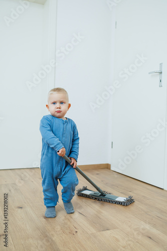 Obraz na płótnie Toddler boy in blue romper cleans the room with a mop. Child washes the floor with a mop. Smiling boy runs around the house and cleans. w salonie