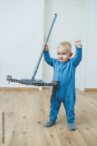 Obraz na płótnie Blond toddler boy washes the floor with a mop, helping his mother clean at home, free space. Child learns to clean the house. w salonie