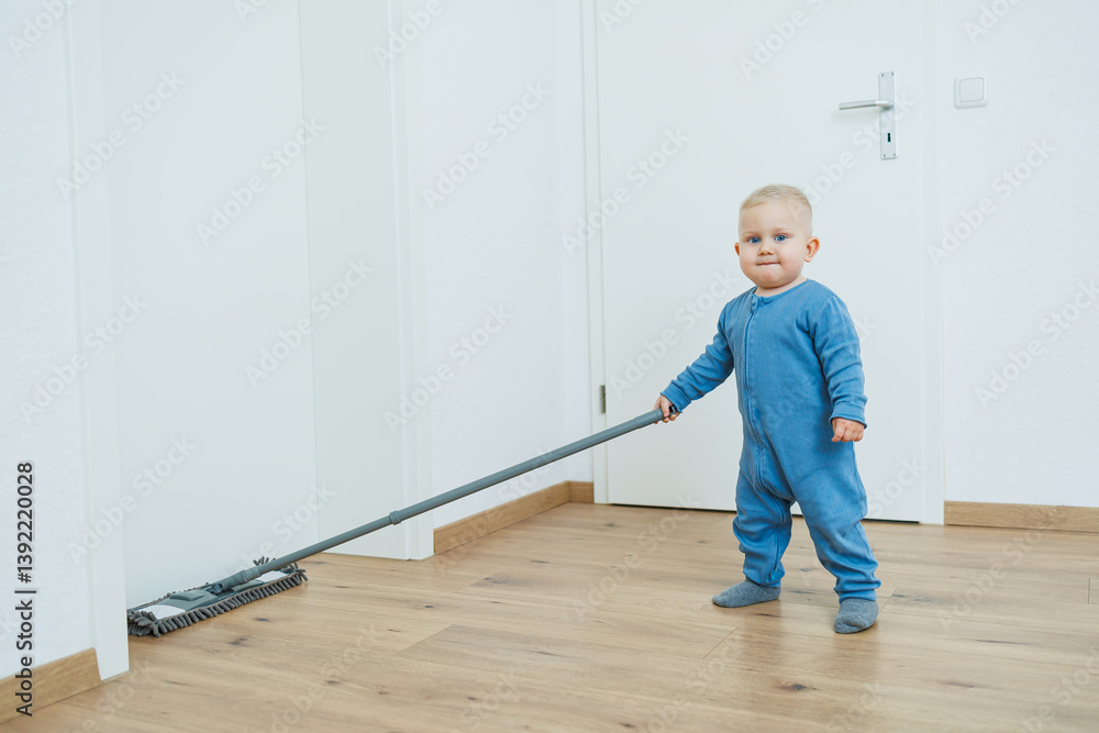Blond toddler boy washes the floor with a mop, helping his mother clean at home, free space. Child learns to clean the house.