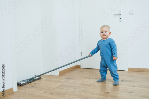 Obraz na płótnie Blond toddler boy washes the floor with a mop, helping his mother clean at home, free space. Child learns to clean the house. w salonie