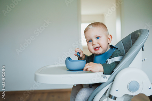 Obraz na płótnie Toddler boy in casual clothes sits at the table in a highchair and eats himself with a spoon. The child learns to eat independently. Healthy nutrition for children. Baby food w salonie