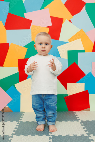 Blue-eyed toddler boy in a white t-shirt and jeans on a bright wall background. Child in stylish casual clothes.