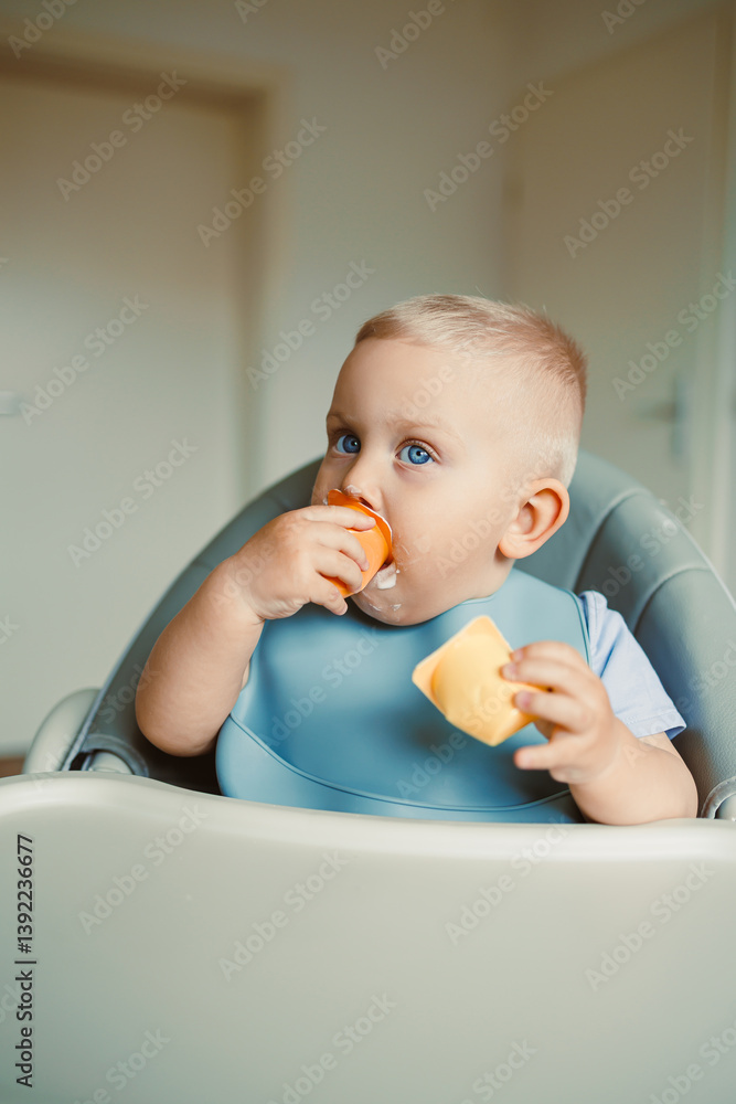 Smiling boy sitting in a high chair, eating yogurt in the kitchen. Healthy food for children. Bio yogurt food for children. Children eating vegetables. Little boy eating dairy products.