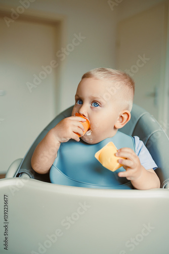 Obraz na płótnie Smiling boy sitting in a high chair, eating yogurt in the kitchen. Healthy food for children. Bio yogurt food for children. Children eating vegetables. Little boy eating dairy products. w salonie