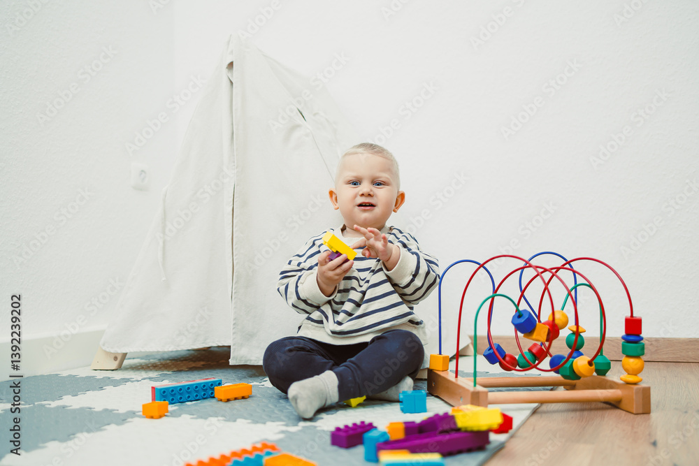 Adorable toddler boy sitting in the living room and playing with educational toys for children. Wooden sorter for child development. Child self-employment. Development of thinking in toddlers.