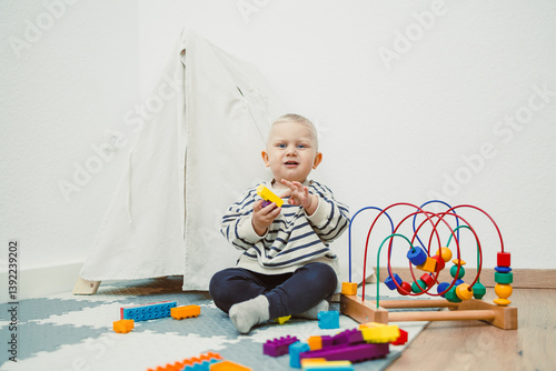 Obraz na płótnie Adorable toddler boy sitting in the living room and playing with educational toys for children. Wooden sorter for child development. Child self-employment. Development of thinking in toddlers. w salonie