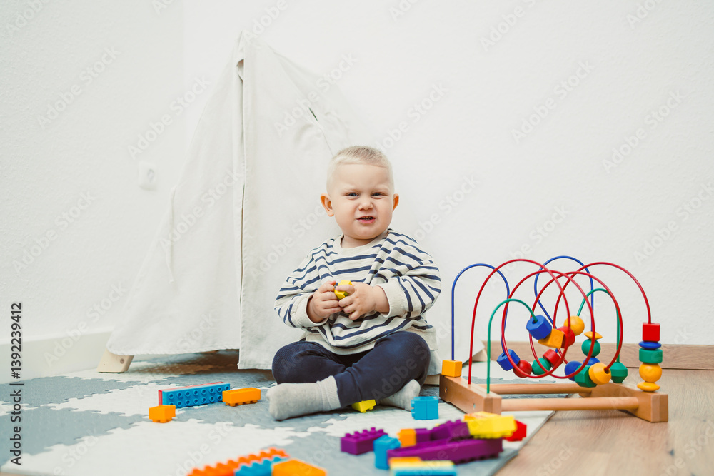 Adorable toddler boy sitting in the living room and playing with educational toys for children. Wooden sorter for child development. Child self-employment. Development of thinking in toddlers.