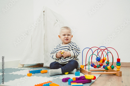 Obraz na płótnie Adorable toddler boy sitting in the living room and playing with educational toys for children. Wooden sorter for child development. Child self-employment. Development of thinking in toddlers. w salonie