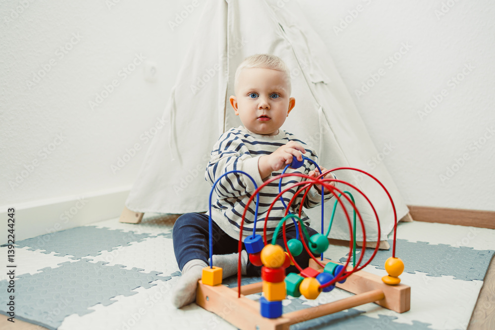 Adorable toddler boy sitting in the living room and playing with educational toys for children. Wooden sorter for child development. Child self-employment. Development of thinking in toddlers.