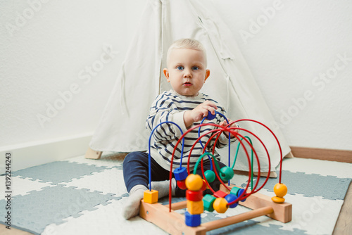 Obraz na płótnie Adorable toddler boy sitting in the living room and playing with educational toys for children. Wooden sorter for child development. Child self-employment. Development of thinking in toddlers. w salonie