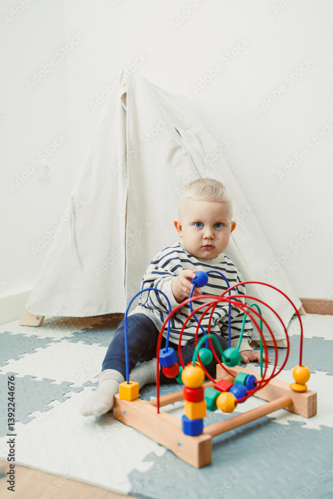 Adorable toddler boy sitting in the living room and playing with educational toys for children. Wooden sorter for child development. Child self-employment. Development of thinking in toddlers.