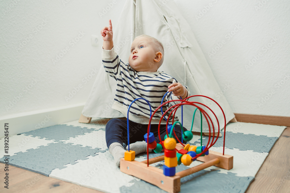 Adorable toddler boy sitting in the living room and playing with educational toys for children. Wooden sorter for child development. Child self-employment. Development of thinking in toddlers.