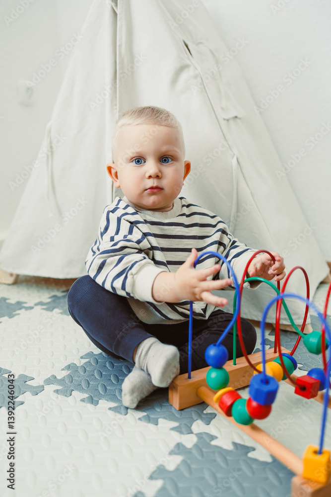 Adorable toddler boy sitting in the living room and playing with educational toys for children. Wooden sorter for child development. Child self-employment. Development of thinking in toddlers.