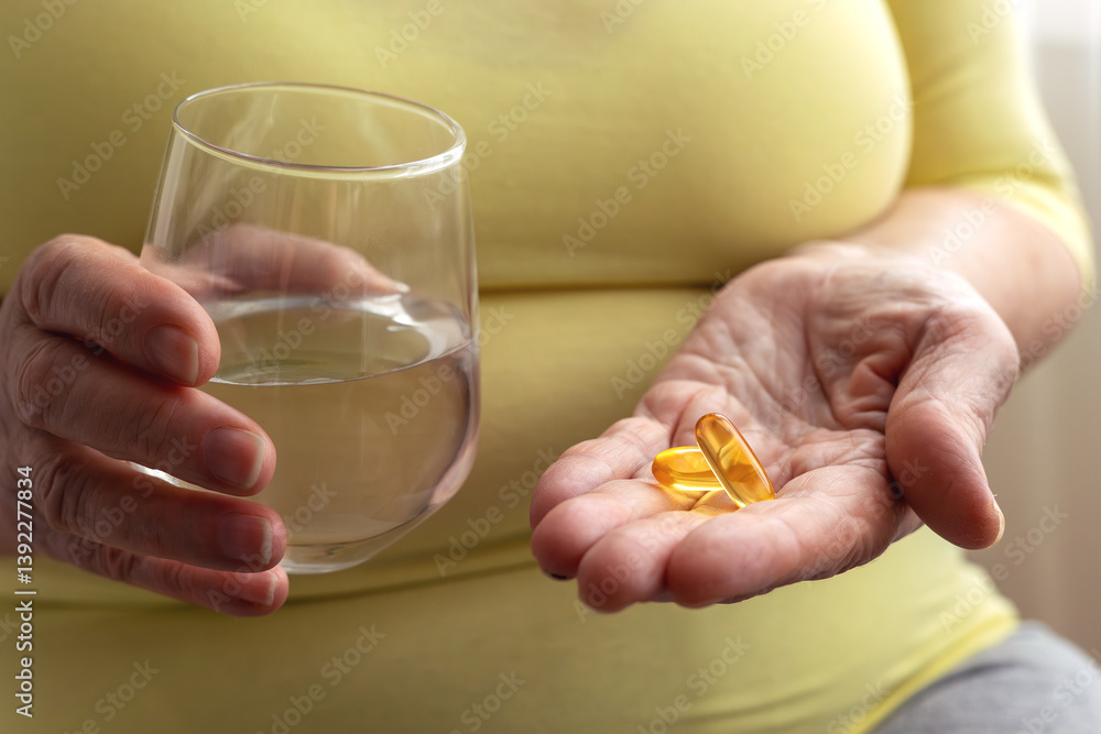 Senior holding water glass and capsules in hand. Health in adulthood, maintaining activity and energy. Disease prevention, use of vitamins and supplements, treatment, pharmaceuticals. Senior holding water glass and capsules in hand. Health in adulthood, maintaining activity and energy. Disease prevention, use of vitamins and supplements, treatment, pharmaceuticals.