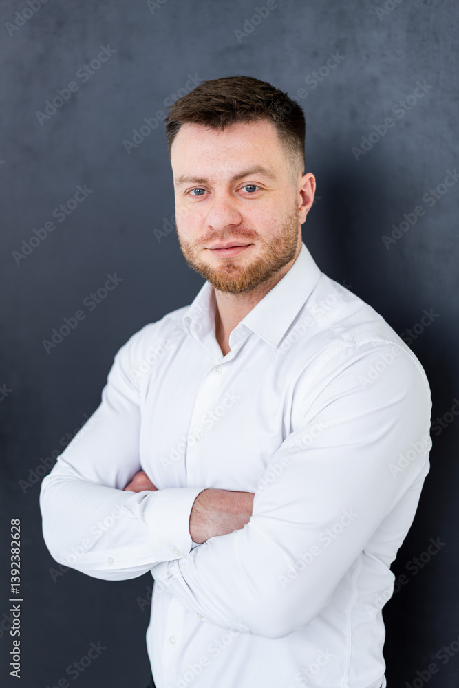 Confident man poses indoors. A confident man with a groomed beard stands with arms crossed in a white shirt against a dark backdrop. Confident man poses indoors. A confident man with a groomed beard stands with arms crossed in a white shirt against a dark backdrop.