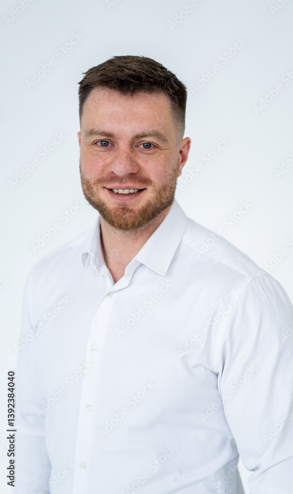 Professional man in white shirt smiling. A man with a well-groomed beard and short hair stands against a plain background, smiling confidently in a white shirt. Professional man in white shirt smiling. A man with a well-groomed beard and short hair stands against a plain background, smiling confidently in a white shirt.