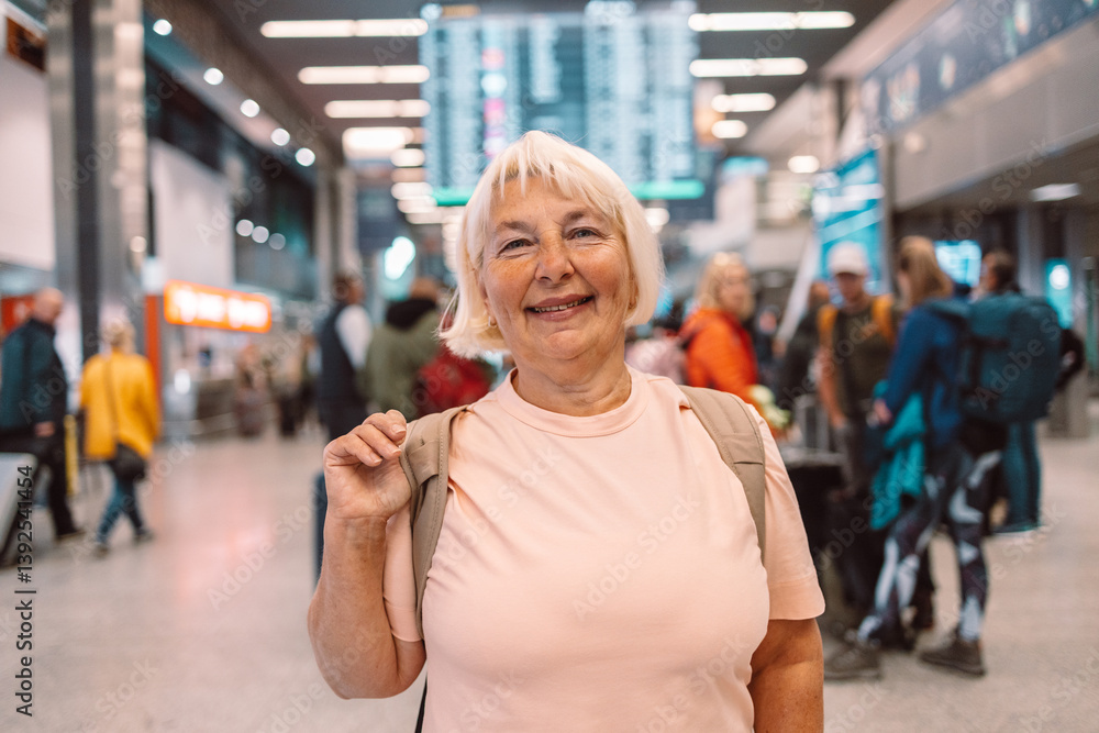 Happy elderly woman in a pink t-shirt with a backpack, smiling at the airport terminal. She ready for her next travel adventure. Ideal for travel, senior lifestyle, and vacation content.